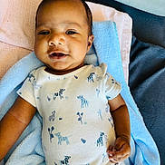 Ryan is registered to the contest to win money with this photo: baby, infant, child, blanket, onesie, clothing, smile, face, skin, hand, blue, white, zebra_pattern, soft_texture, cute, lying_down, portrait, indoors, happy, young