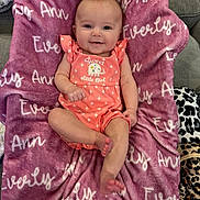 Everly joined the competition — help win amazing prizes! baby, infant, smiling, pink_outfit, blanket, text, couch, indoor, cute, child, face, person, leopard_print, plush_blanket, happy, comfort, portrait, sitting, soft_texture, cozy