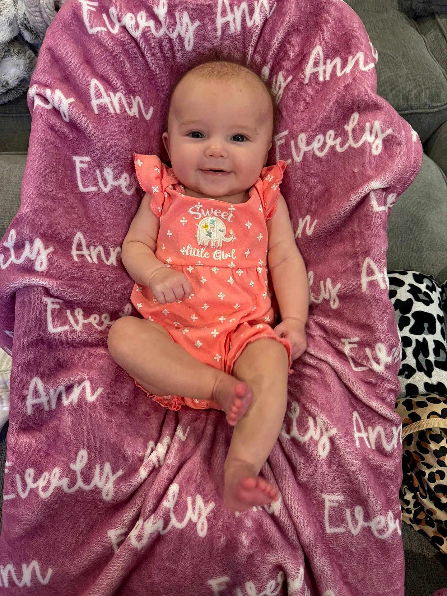 Everly joined the competition — help win amazing prizes! baby, infant, smiling, pink_outfit, blanket, text, couch, indoor, cute, child, face, person, leopard_print, plush_blanket, happy, comfort, portrait, sitting, soft_texture, cozy