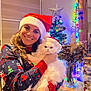 Mili joined the competition — help win amazing prizes! woman, cat, santa_hat, holiday_sweater, christmas_tree, string_lights, vase, dried_flowers, jar, ornaments, table, smile, indoor, festive, decorations, portrait, white_cat, holding, happy, cozy
