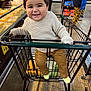 aisle, baby, cart, child, floor, food, grocery_store, happy, indoor, pants, people, person, products, retail, shoes, shopping_cart, smiling, store_shelf, sweater, toddler