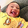 baby, smiling, laughing, yellow_clothing, tshirt, tigger, piglet, child, cute, happy, infant, face, portrait, person, indoors, couch, fabric, closeup, skin, cheerful