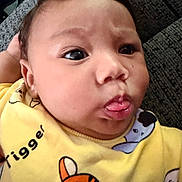 Zayvion is registered to the contest to win money with this photo: baby, face, tongue, yellow_clothing, cartoon, closeup, child, infant, cute, expression, person, portrait, texture, fabric, indoors, head, skin, eyebrows, hand, sleeve