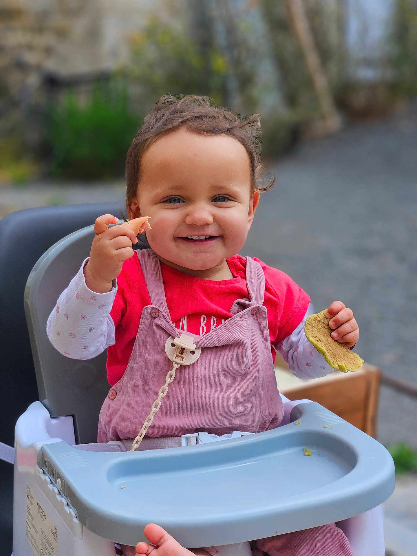 Odélya participe au concours pour gagner de l'argent avec cette photo : toddler, child, high_chair, smiling, food, outdoor, happy, face, person, clothing, pink_overalls, red_shirt, hands, seat, baby, cute, portrait, daylight, young_child, playful
