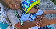 Giovanni is registered to the contest to win money with this photo: child, baby, smile, hat, sunglasses, chair, outdoor, grass, concrete, clothing, holding, happy, cute, sunlight, playing, toddler, hand, blue, summer, friends