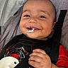baby, child, smile, face, hand, car_seat, seatbelt, red_clothing, black_clothing, spider_web_design, food, messy, closeup, infant, happy, cute, portrait, indoors, young_child, baby_clothes