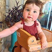 Ambre a rejoint le concours — aidez-le/la à gagner de superbes lots ! toddler, child, baby, high_chair, wooden_chair, curious, indoors, plant, potted_plant, stone_wall, brown_hair, casual_clothing, sleeveless_top, reaching_hand, expression, face, portrait, cute, young_child, natural_light