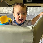 Miguel joined the competition — help win amazing prizes! baby, child, toy, playpen, curly_hair, indoor, living_room, furniture, television, expression, joyful, curious, clothing, mesh, hand, face, head, person, infant, soft