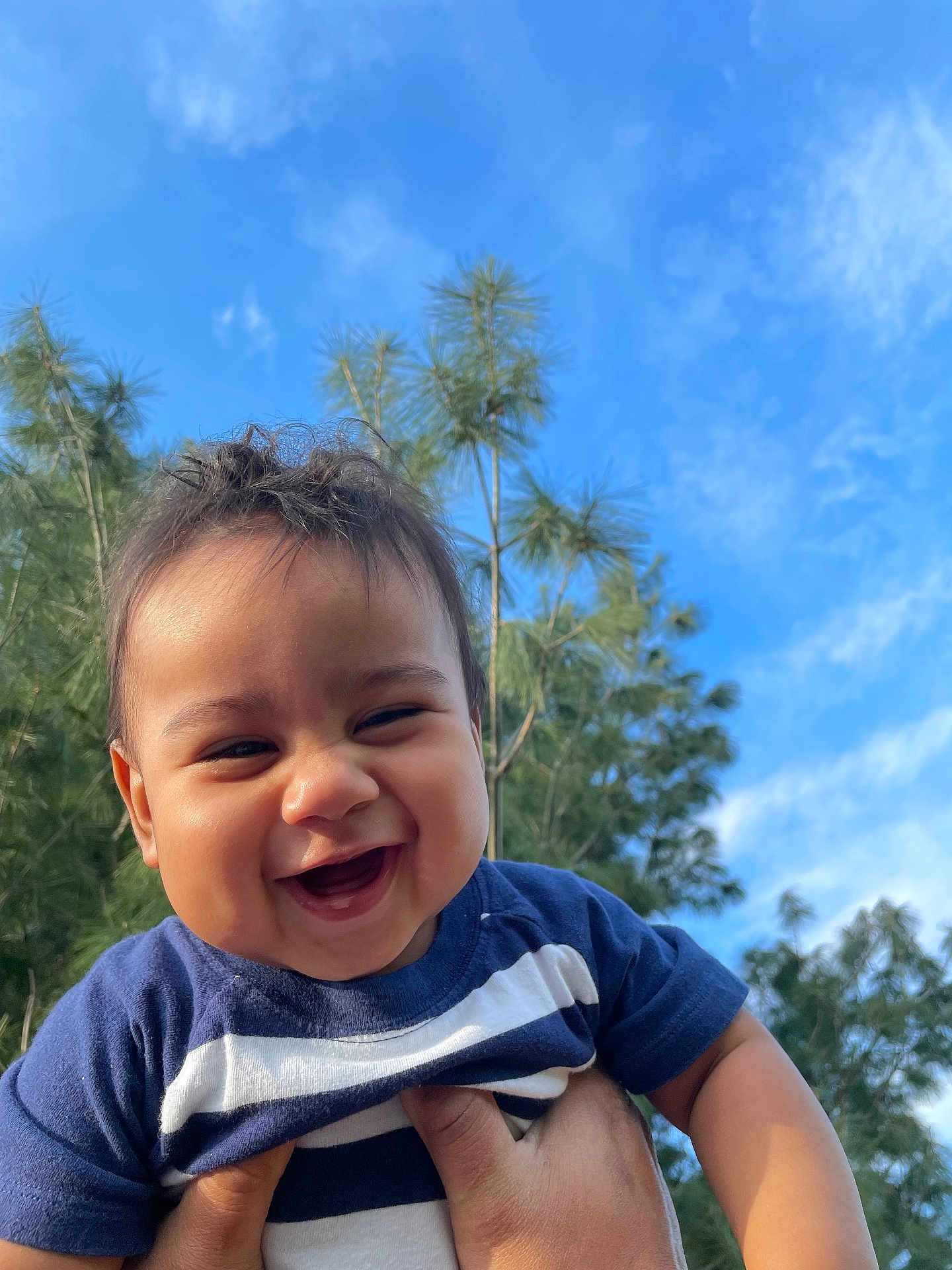 Matteo is registered to the contest to win money with this photo: baby, smiling, child, outdoor, sky, blue_sky, trees, greenery, happy, person, face, holding, toddler, short_hair, casual_clothing, blue_shirt, daylight, nature, portrait, cute