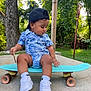 toddler, child, skateboard, backwards_cap, white_sneakers, blue_outfit, outdoor, greenery, trees, concrete, grass, summer, young_child, casual_clothing, cap, playful, cute, side_profile, sunlight, nature