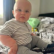 Cohen joined the competition — help win amazing prizes! baby, child, indoor, bed, striped_shirt, gray_pants, remote_control, blue_eyes, sitting, cute, plush, soft_focus, patterned_bedspread, cozy, curious, person, clothing, furniture, room, portrait