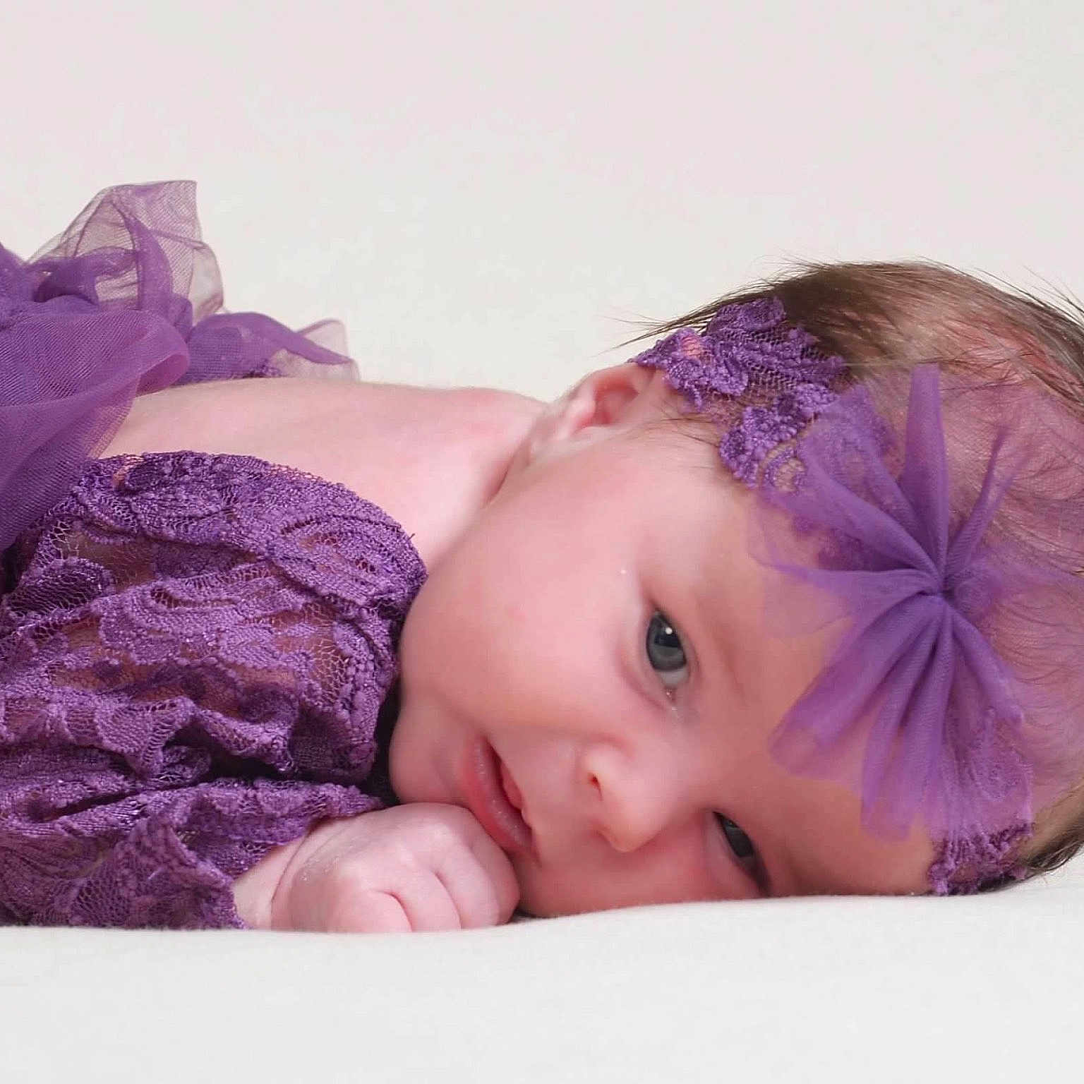 Lilyann is registered to the contest to win money with this photo: baby, infant, purple_lace, headband, tulle_bow, lying_down, soft_gaze, newborn, cute, portrait, closeup, delicate, skin, hand, face, child, young, sleepy, fabric, light_background