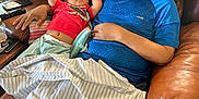Cailoren is registered to the contest to win money with this photo: baby, man, sleeping, couch, leather, blanket, living_room, relaxing, child, adult, casual_clothing, red_shirt, blue_shirt, home, resting, comfort, pillow, hand, indoor, nap