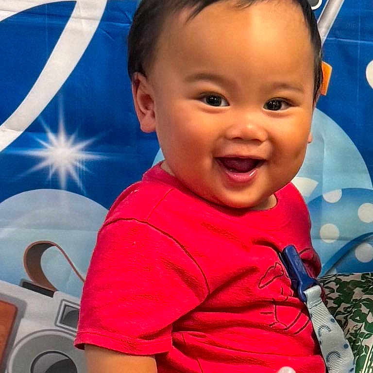 Cailoren is registered to the contest to win money with this photo: baby, background, cheerful, child, clothing, colorful, cute, expression, face, hand, happy, holding, indoor, infant, pacifier, person, portrait, red_shirt, smiling, young_child