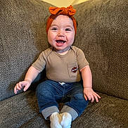 Eleanor is registered to the contest to win money with this photo: baby, infant, smiling, headband, bow, couch, sofa, sitting, portrait, happy, onesie, jeans, socks, living_room, cute, chubby_cheeks, hands, face, cozy, furniture