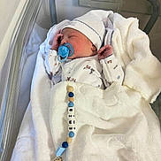 Jamiletze is registered to the contest to win money with this photo: newborn, baby, pacifier, blanket, hat, hospital_bassinet, sleeping, infant, clothing, beads, clip, cute, cozy, resting, child, indoors, person, white, soft, peaceful