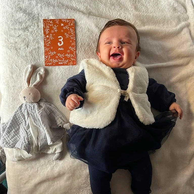 Alya participe au concours pour gagner de l'argent avec cette photo : baby, baby_sleeping, baby_toddler_clothing, bedding, comfort, finger, gesture, hairstyle, happy, human, linens, pattern, person, sitting, skin, sleeve, smile, textile, toddler, vertebrate