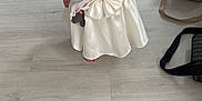 Catalina participe au concours pour gagner de l'argent avec cette photo : bag, barefoot, child, curious, dress, floor, furniture, girl, home, indoor, light, pacifier, person, pigtails, shelf, standing, toddler, toy, white_dress, wooden_floor
