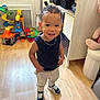 Braydenn participe au concours pour gagner de l'argent avec cette photo : toddler, child, smiling, standing, curly_hair, sneakers, pants, tank_top, indoor, wooden_floor, toys, playroom, furniture, cabinet, chain_necklace, happy, person, young_child, casual_clothing, home