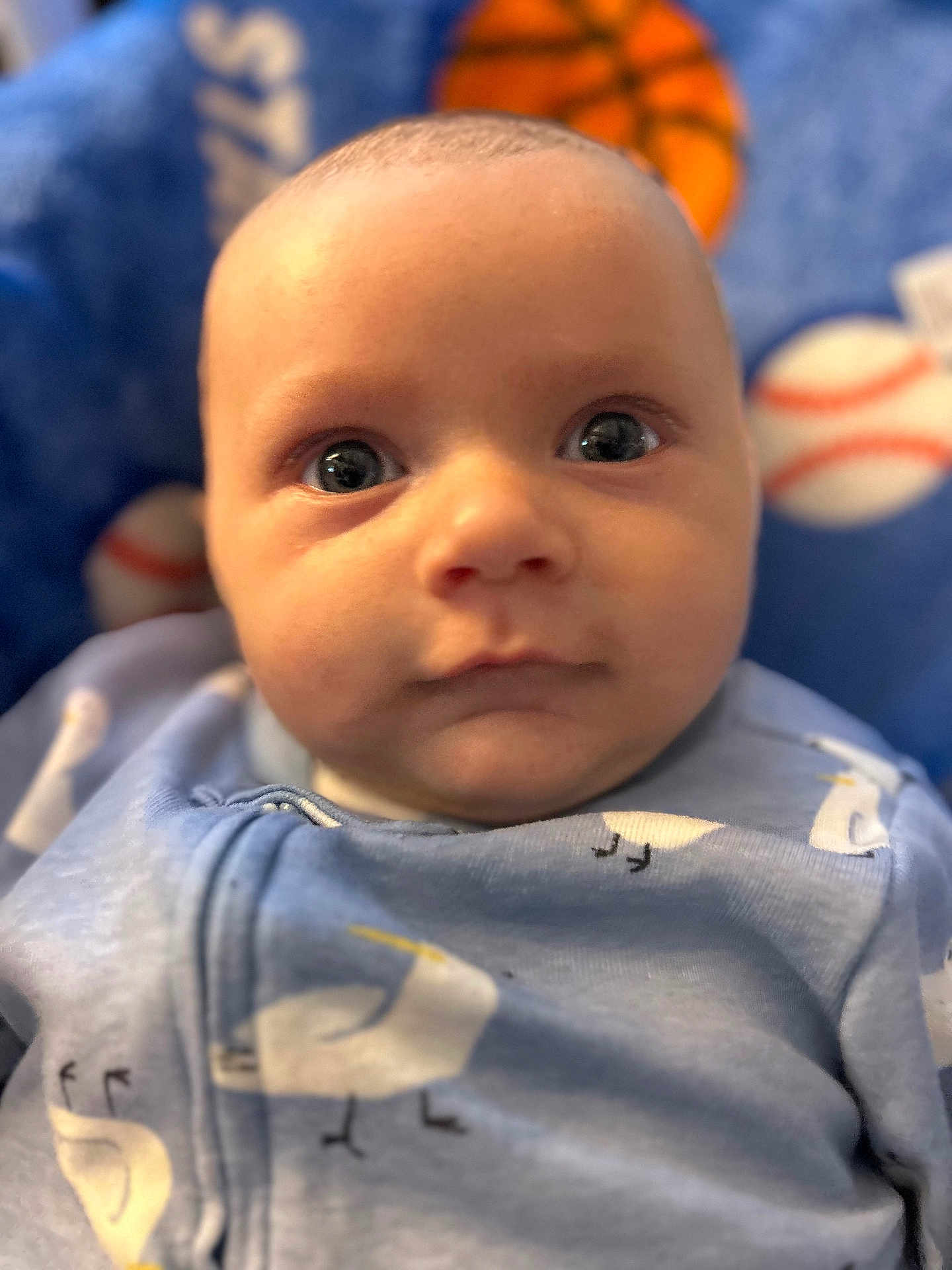 Ashtyn is registered to the contest to win money with this photo: baby, infant, face, eyes, blue_onesie, bird_pattern, close_up, portrait, child, soft_focus, indoor, cute, newborn, skin, expression, young_child, background_blur, sports_theme, blanket, comfort