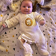 Sacha participe au concours pour gagner de l'argent avec cette photo : baby, infant, onesie, blanket, stuffed_animal, plush_toy, smiling, face, person, soft_texture, quilted, lying_down, cute, indoors, child, animal_toy, sleepwear, cozy, patterned_blanket, warm_lighting