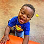 O'Mari is registered to the contest to win money with this photo: child, toddler, smiling, blue_shirt, airplane_graphic, orange_cushion, indoor, play_area, happy, laughing, hands, curly_hair, skin, short_sleeves, floor, toy, bright_colors, person, cute, joy