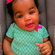 Eli'Yana is registered to the contest to win money with this photo: baby, child, smiling, curly_hair, pink_bows, green_outfit, sitting, padded_seat, infant, cute, adorable, portrait, indoors, person, young_child, hand, face, bright_colors, happy, closeup