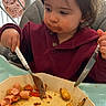 toddler, child, high_chair, fork, knife, food, meal, gnocchi, sausage, plate, messy_face, eating, indoor, clothing, red_sweater, table, baby, person, cute, dinner