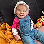 baby, blanket, child, clothing, couch, cozy, cute, denim_overalls, face, happy, indoor, infant, person, pink_shirt, plush_toy, portrait, seated, smiling, soft_toys, white_hat