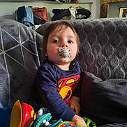 Eiji a rejoint le concours — aidez-le/la à gagner de superbes lots ! baby, child, colorful, couch, cute, furniture, gray_blanket, home, indoor, living_room, pacifier, person, playtime, portrait, relaxed, seated, superman_shirt, toddler, toys, young_child