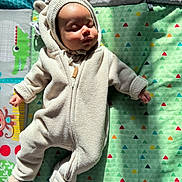 Kaleela is registered to the contest to win money with this photo: baby, sleeping, onesie, bear_ears, plush, cozy, play_mat, colorful, animal_pattern, geometric_pattern, sunlight, soft_lighting, infant, cute, child, indoor, peaceful, portrait, warm, resting