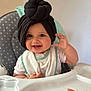 baby, child, high_chair, bib, smile, hand, face, headwrap, turban, toy, flower, indoor, person, cute, happy, infant, clothing, seat, polka_dot, feeding