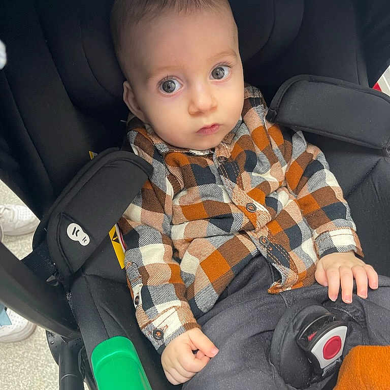 Thélio a rejoint le concours — aidez-le/la à gagner de superbes lots ! baby, black_cushion, buttoned_shirt, casual_clothing, child, curious, cute, face, green_bottle_holder, hands, indoor, infant, orange_booties, plaid_shirt, portrait, seat_belt, seated, stroller, wide_eyes, young_child