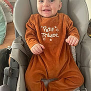 Thélio a rejoint le concours — aidez-le/la à gagner de superbes lots ! baby, baby_chair, child, comfort, cozy, cute, face, happy, home, indoor, infant, onesie, orange_clothing, person, plush, seat, sitting, small_hands, smile, teeth