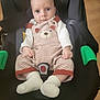 baby, child, car_seat, striped_clothing, bear_design, white_socks, indoor, black_seat, green_armrests, infant, person, cute, portrait, looking_at_camera, small_hands, sitting, floor, wooden_floor, clothing, baby_clothes