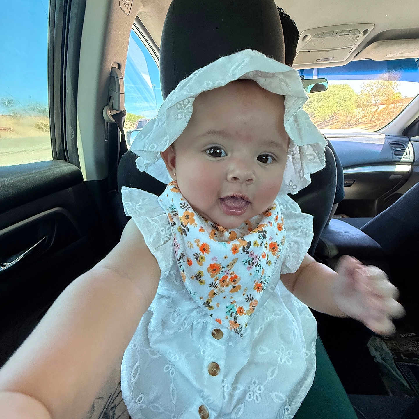 Arya joined the competition — help win amazing prizes! baby, car_interior, car_seat, child, closeup, cute, daylight, floral_bib, happy, hat, infant, person, portrait, reaching_hand, seat, smiling, sunlight, travel, white_clothing, window