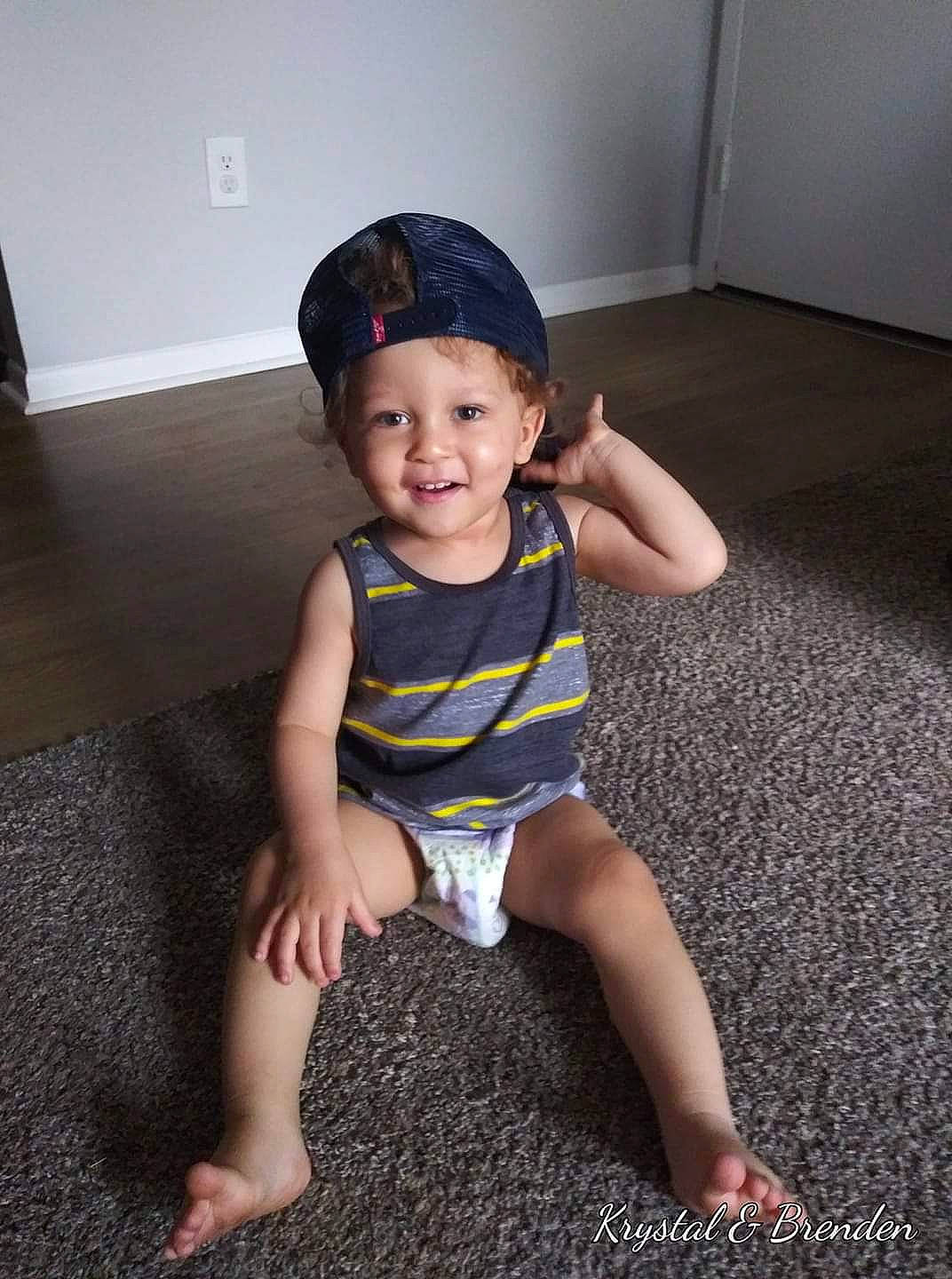 Brenden is registered to the contest to win money with this photo: baby, baby_toddler_clothing, baseball_cap, cap, chin, eye, face, flash_photography, floor, flooring, happy, hat, head, headwear, human_body, joy, person, shoulder, sleeve, smile