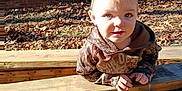Beau is registered to the contest to win money with this photo: autumn, baby, blue_eyes, brick_wall, camouflage, child, curious, daylight, hoodie, leaves, nature, outdoor, person, playful, portrait, sunlight, toddler, windows, wooden_planks, young_child