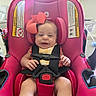 Emily is registered to the contest to win money with this photo: baby, child, car_seat, pink, bow, smiling, safety_harness, indoors, window_blinds, face, person, seat, cute, infant, clothing, happy, head, legs, room, photography