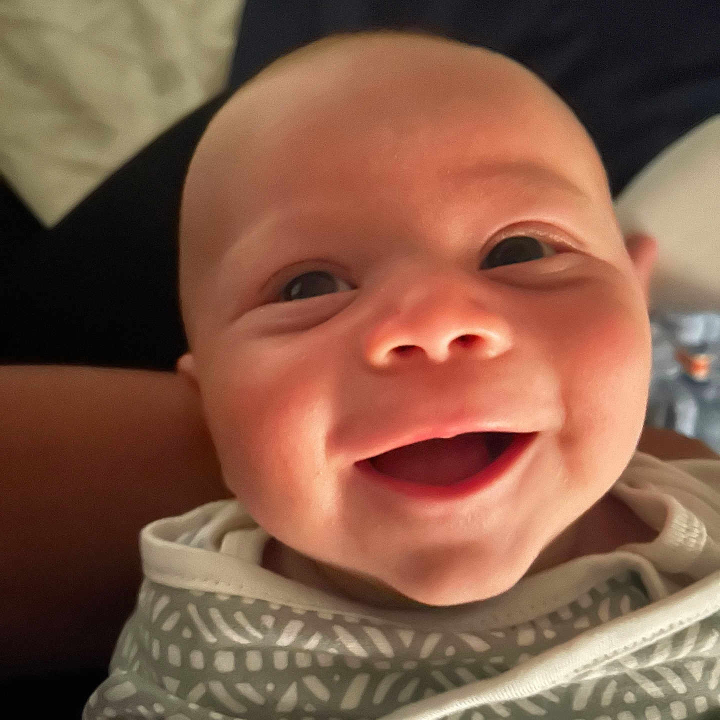 Gunter is registered to the contest to win money with this photo: baby, child, close_up, cute, eyes, face, happy, head, human, indoors, infant, mouth, newborn, patterned_clothing, person, portrait, skin, smile, soft_light, swaddle