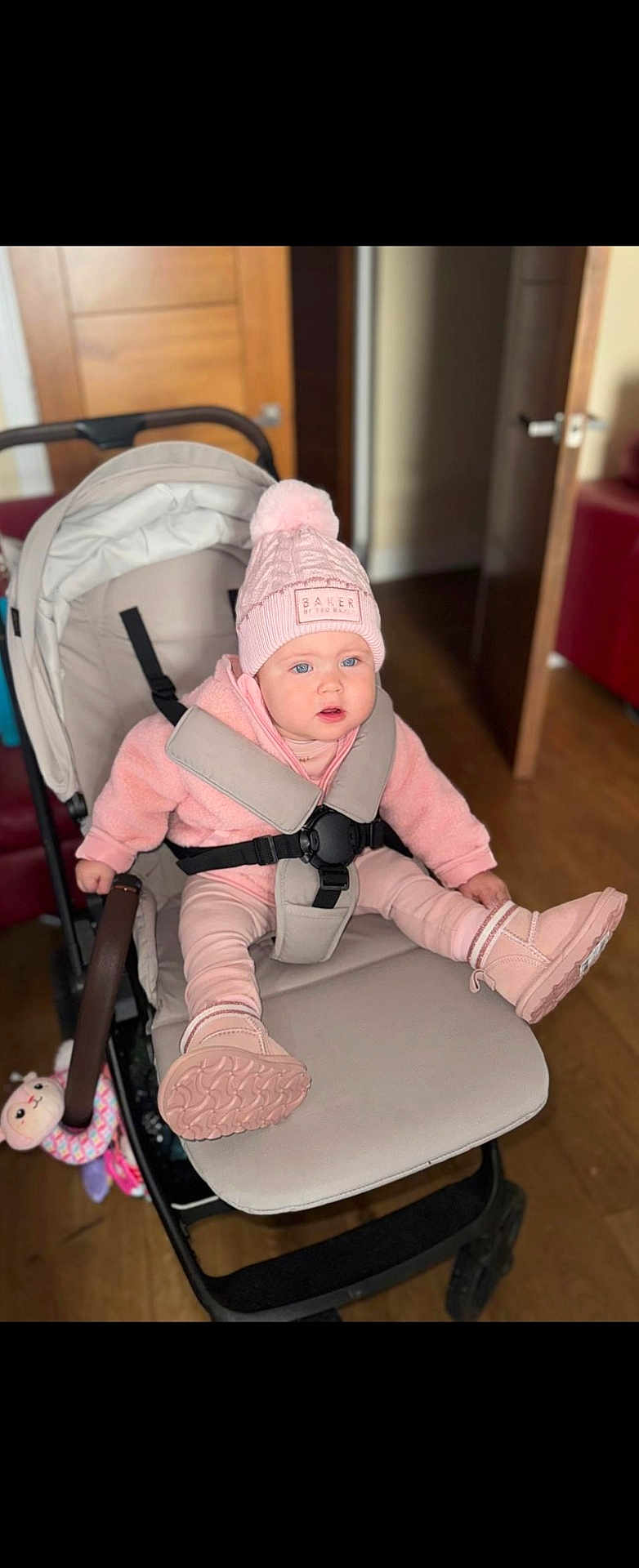 Sharon-Antonia joined the competition — help win amazing prizes! baby, child, stroller, pink_clothing, hat, pom_pom, boots, indoor, wooden_floor, door, straps, seat, curious_expression, face, person, baby_toy, warm_clothing, hoodie, cushion, baby_seat