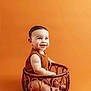 baby, infant, smiling, wicker_basket, orange_background, cute, child, portrait, sitting, happy, studio, one_person, young, indoors, clothing, skin, face, eyes, mouth, toes
