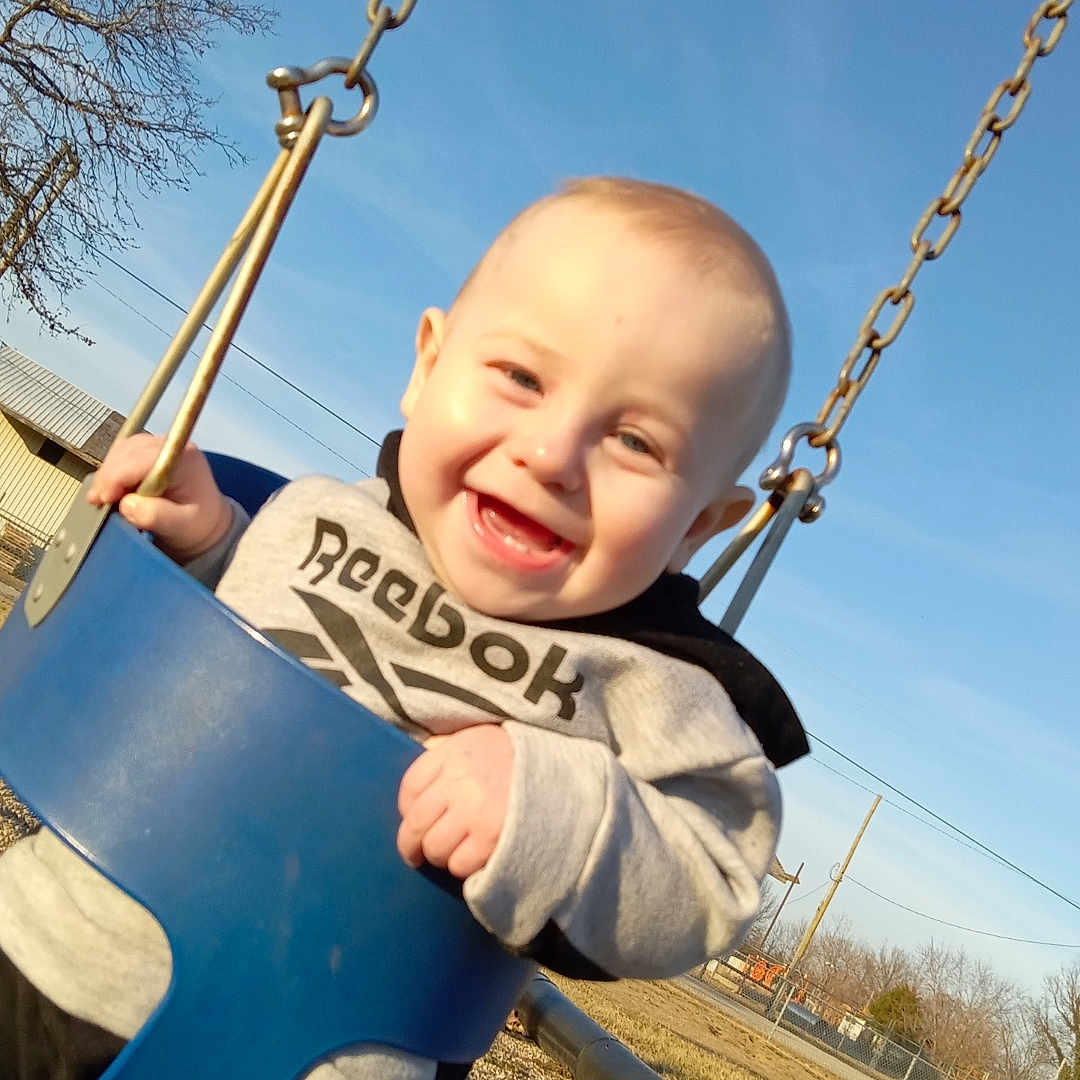 Javarious is registered to the contest to win money with this photo: baby, blue_swing, child, clothing, daylight, fun, grass, happy, infant, joy, outdoor, park, person, playground, recreation, sky, smiling, sunlight, swing, trees