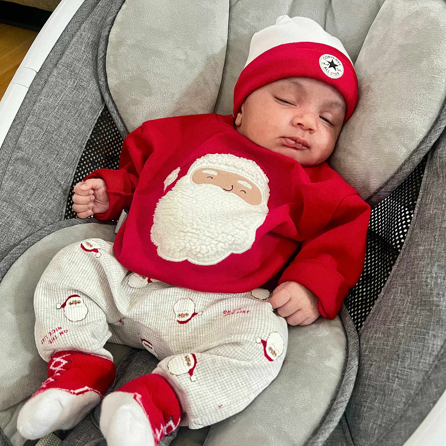 Dariel is registered to the contest to win money with this photo: baby, baby_rocker, child, cozy, cushion, cute, festive, footwear, gray_fabric, hat, holiday, indoors, infant, peaceful, red_clothing, relaxing, santa_clothing, sleeping, smiling_face_on_clothing, sock
