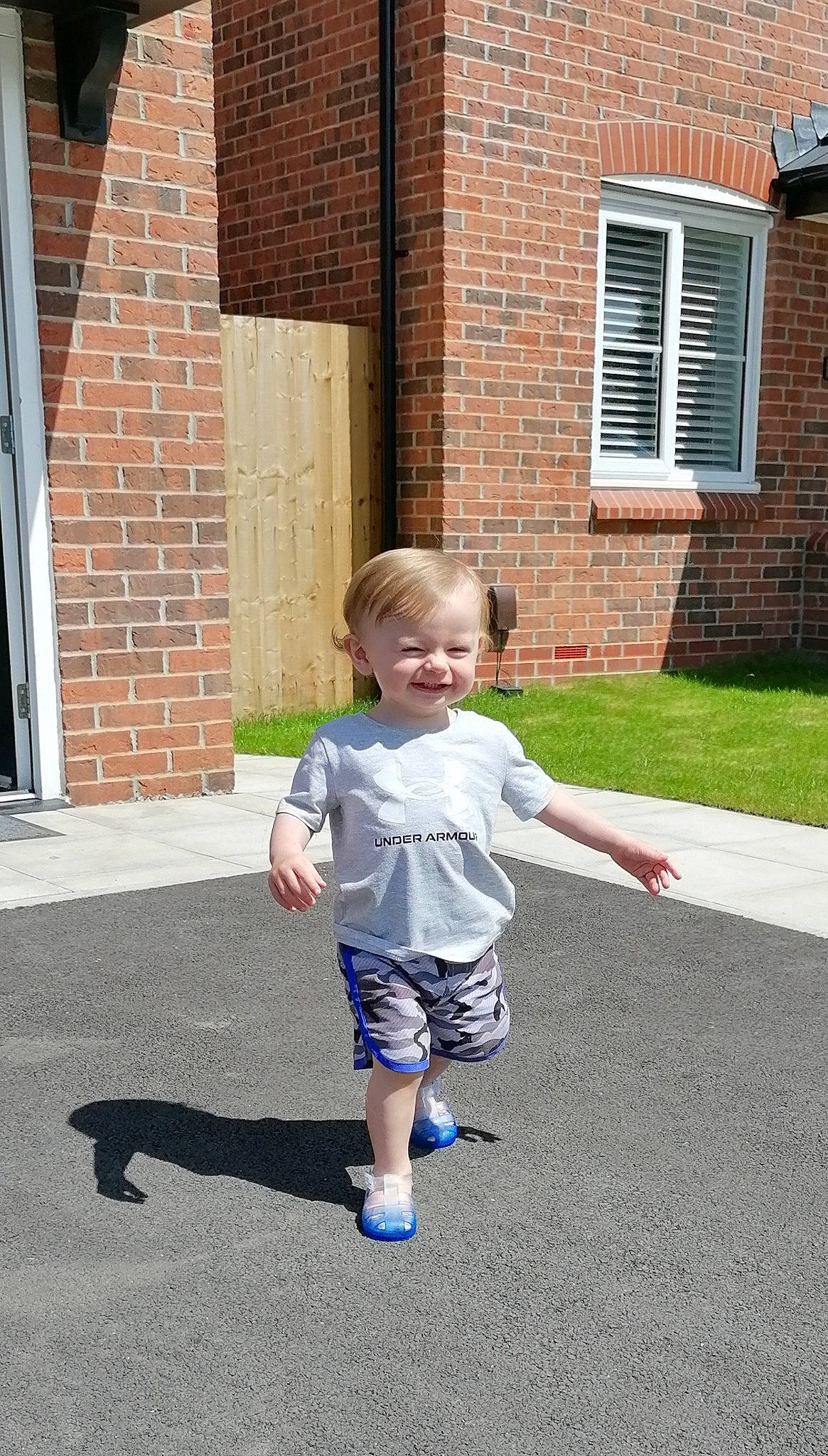 Markus is registered to the contest to win money with this photo: asphalt, baby, brick, brickwork, child, door, driveway, flooring, fun, grass, happy, joy, leisure, person, road_surface, shorts, sidewalk, smile, standing, t_shirt