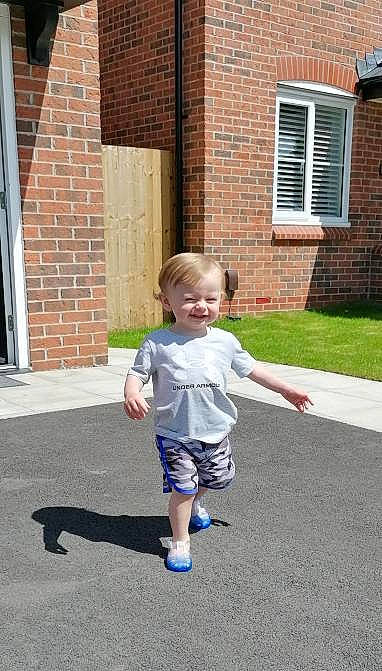 Markus is registered to the contest to win money with this photo: asphalt, baby, brick, brickwork, child, door, driveway, fun, grass, joy, leisure, person, recreation, road_surface, shorts, sidewalk, sleeve, smile, standing, t_shirt