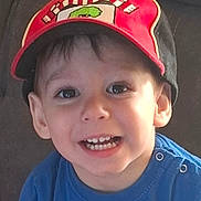 Liam a rejoint le concours — aidez-le/la à gagner de superbes lots ! blue_shirt, boy, bright_eyes, cap, casual_clothing, child, childhood, cute, expression, face, happy, headwear, indoors, person, portrait, red_cap, sitting, smiling, teeth, young_child