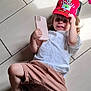 Liam participe au concours pour gagner de l'argent avec cette photo : cap, casual_clothing, child, colorful_sneakers, cute, footwear, happy, indoor, laying_down, pink_toy, playful, red_hat, shorts, smartphone_case, smiling, tile_floor, toddler, toy, white_tshirt, young_child
