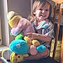 child, smile, plush_toy, chair, wooden_chair, window_light, indoor, happy, toddler, toy, colorful, person, cute, hair, seat, playful, cozy, furniture, young_child, casual_clothing