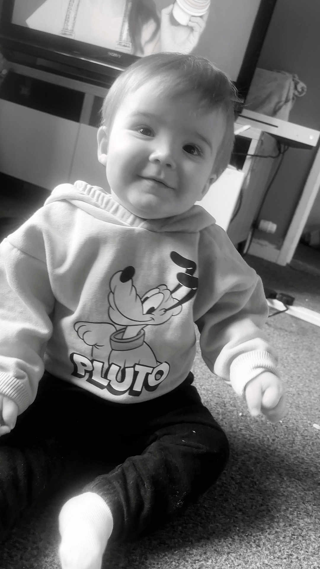 Theo joined the competition — help win amazing prizes! baby, child, smiling, hoodie, pluto, cartoon_character, sitting, indoor, carpet, television, furniture, black_and_white, cute, person, clothing, young_child, happy, portrait, floor, casual